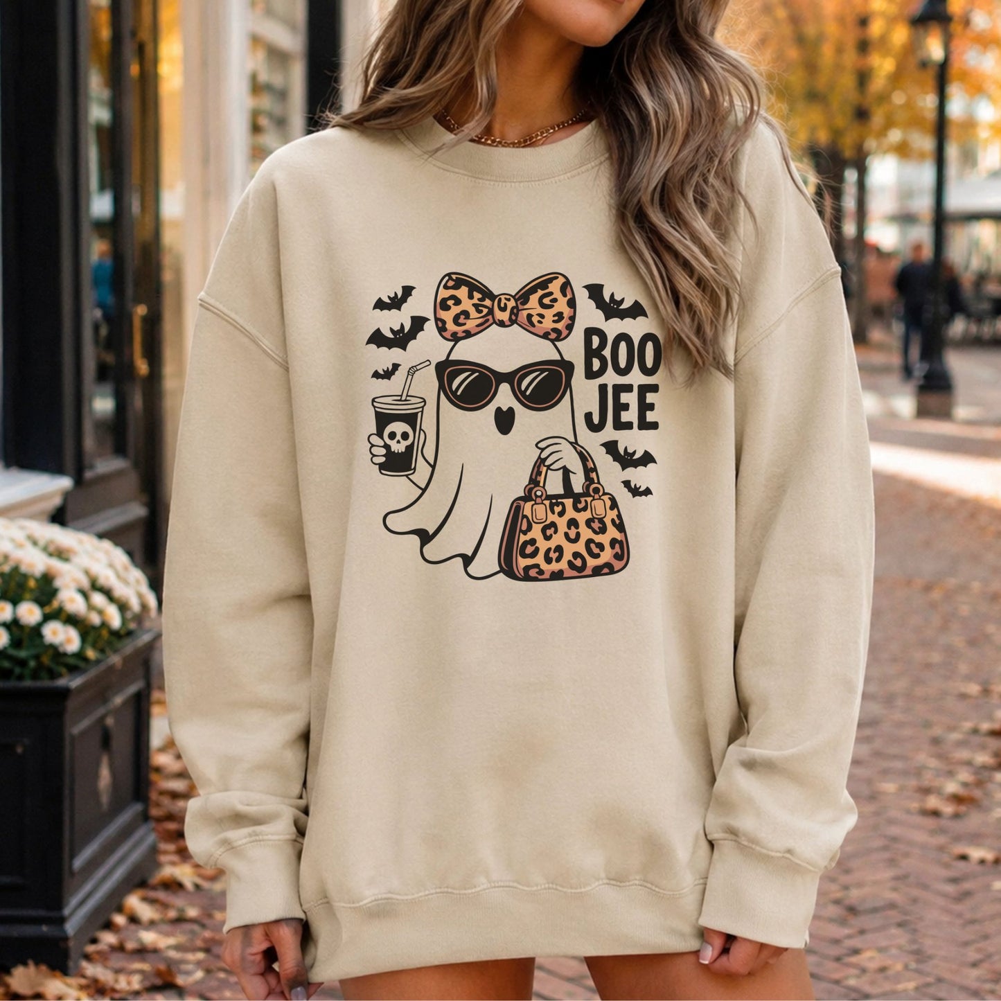 Boo Jee Halloween DTF transfer featuring a fashionable ghost wearing sunglasses with a leopard print bow and matching handbag, holding a spooky coffee cup and surrounded by black bats on a cream sweatshirt mockup.