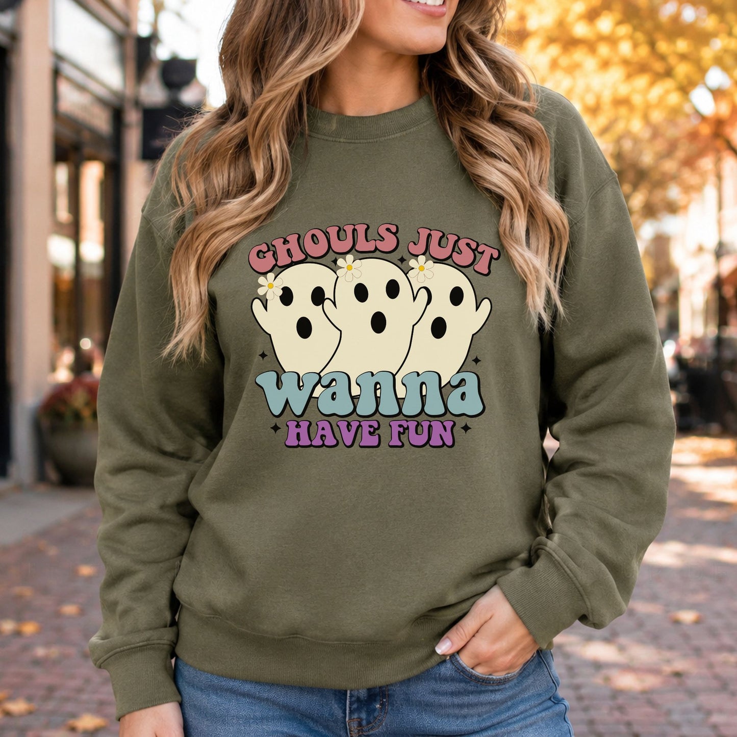 Retro Halloween DTF transfer featuring three cute cream-colored ghosts with daisy accents and the phrase Ghouls Just Wanna Have Fun in pink, blue and purple lettering on an olive green sweatshirt mockup.