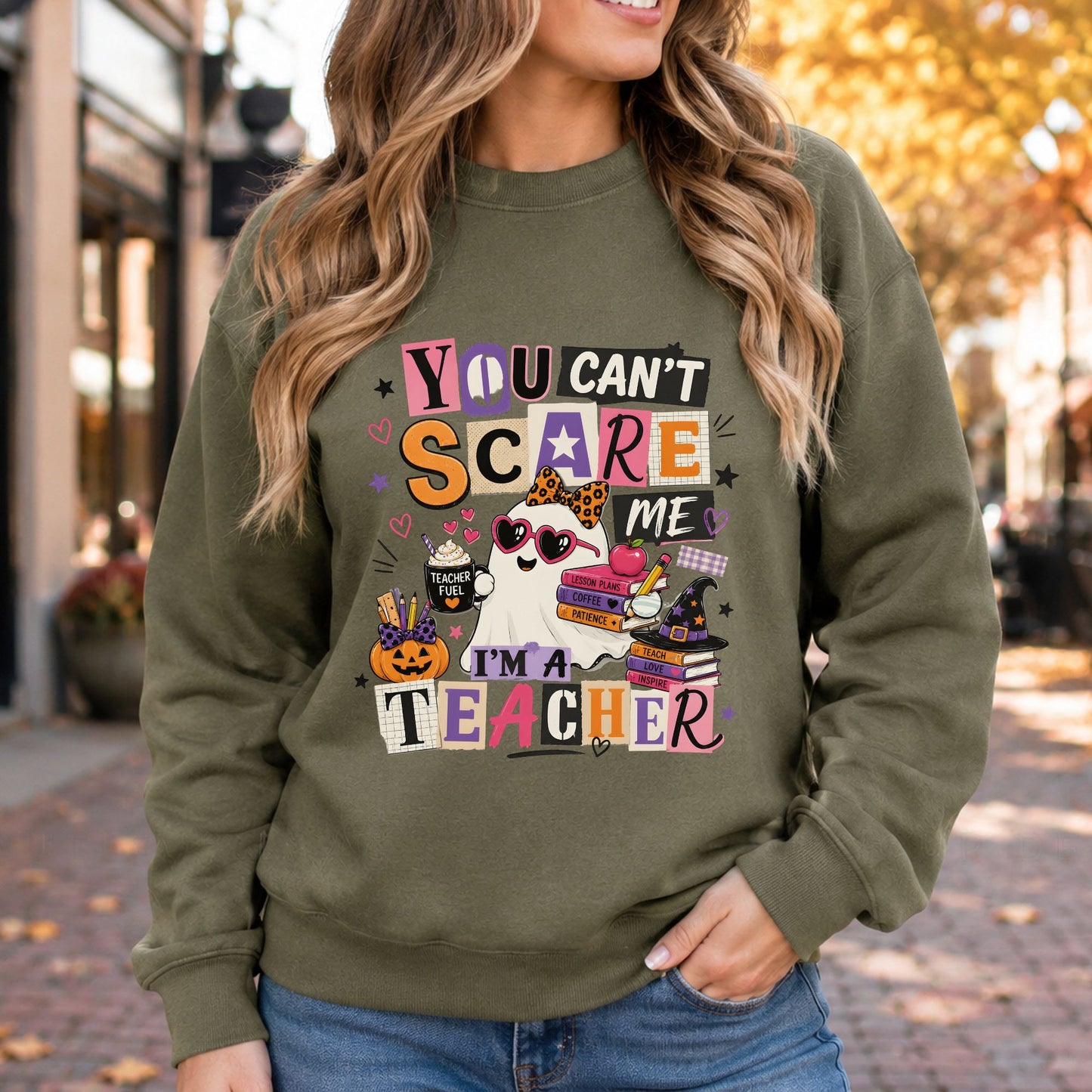 You Can’t Scare Me I’m a Teacher Halloween DTF transfer featuring a cute sheet ghost wearing heart-shaped sunglasses and a leopard-print bow, holding a Teacher Fuel coffee cup beside lesson-plan books, pencils, a jack-o’-lantern and witch hat, with colorful retro lettering on an olive green sweatshirt mockup.