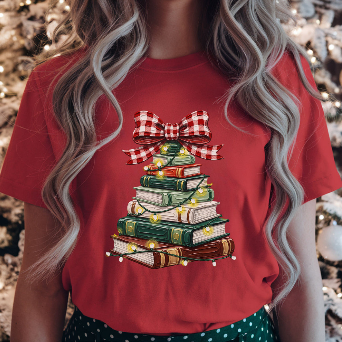 Green, red, cream and brown books stacked into a Christmas tree, wrapped in glowing string lights and topped with a large red and white gingham bow.