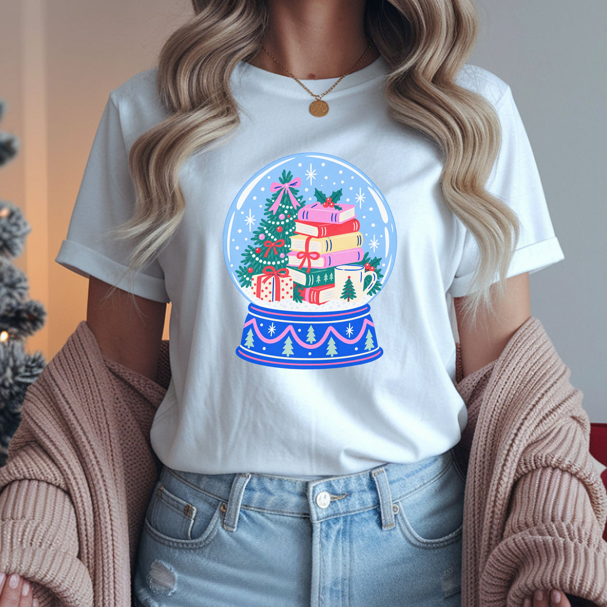 Blue snow globe containing a decorated Christmas tree, colorful stacked books tied with a red bow, a cream mug and a wrapped gift, with pink trim on the base.