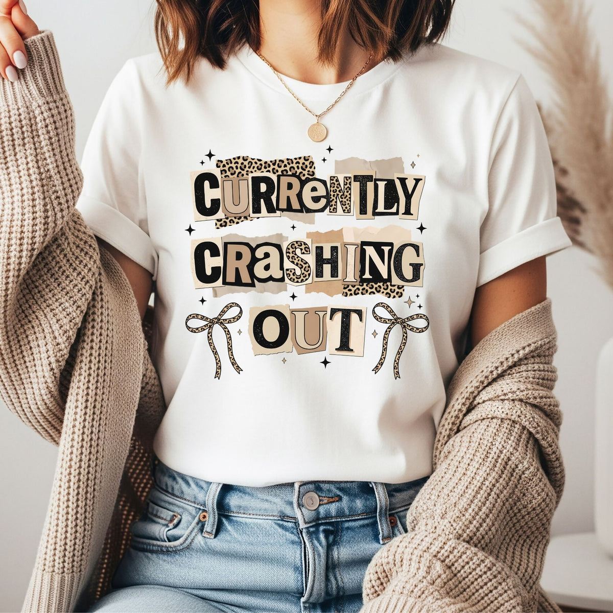 Funny "Currently Crashing Out" graphic featuring leopard print ransom-style lettering with bows and sparkles. Perfect for sarcastic graphic tees, hoodies, trendy apparel, and mental health humor.