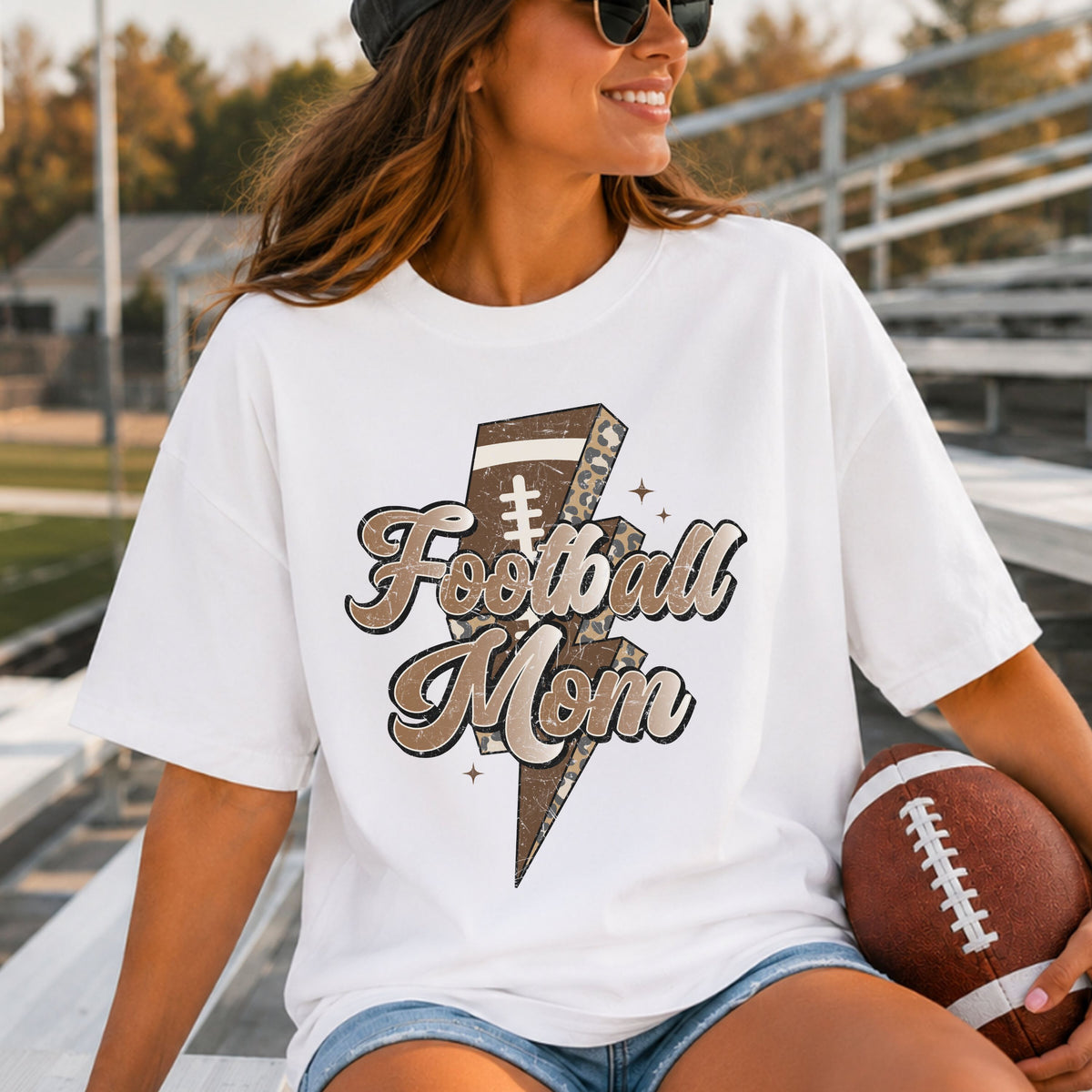 Football Mom DTF transfer featuring large retro script lettering over a brown football lightning bolt with leopard print accents and neutral sparkle details.
