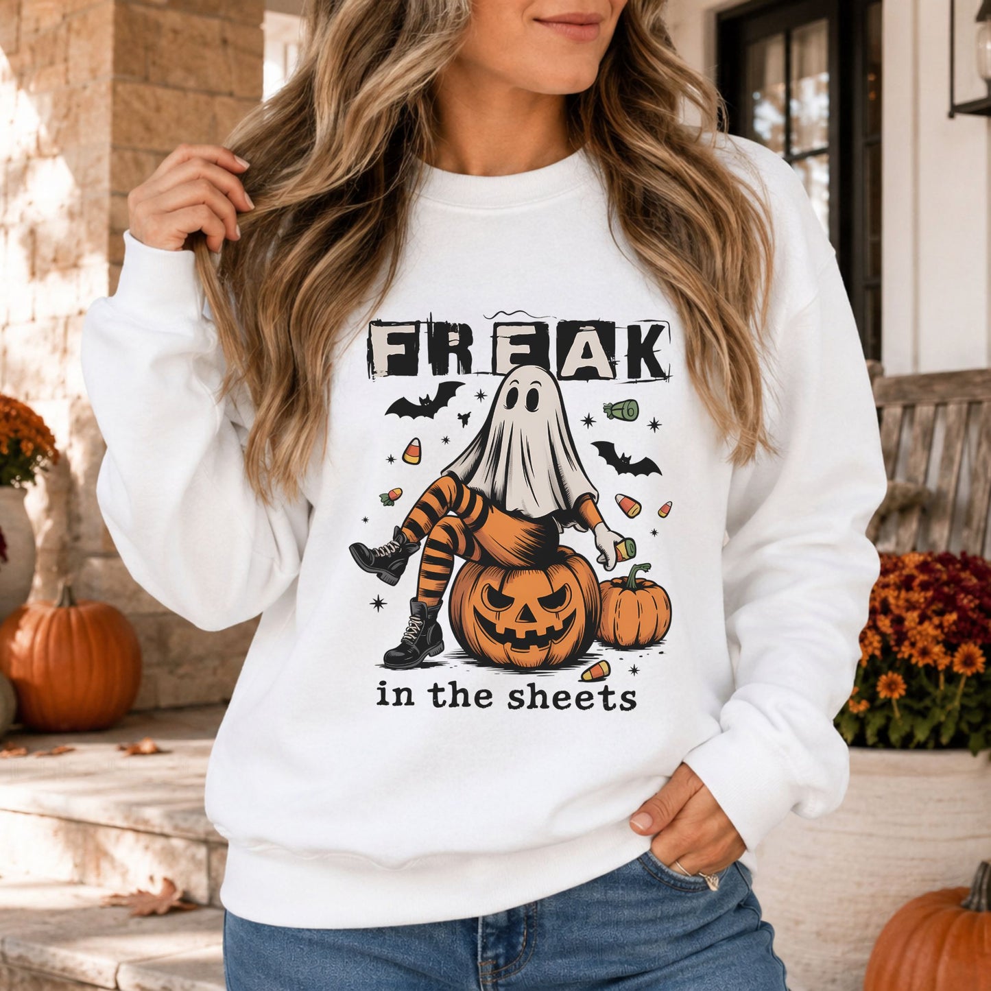 Freak in the Sheets Halloween DTF transfer featuring a sheet ghost sitting on a jack-o-lantern while wearing orange striped tights and black boots, surrounded by candy corn, bats and pumpkins on a white sweatshirt mockup.