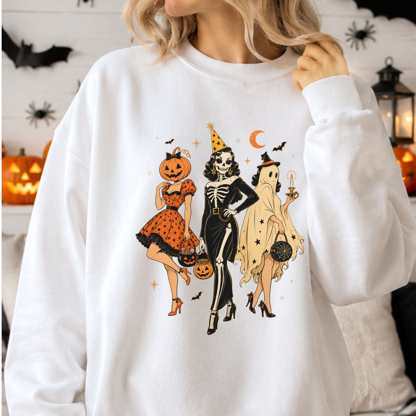 Vintage Halloween DTF transfer featuring three glamorous pinup girls dressed in jack-o-lantern, skeleton and sheet ghost costumes with trick-or-treat buckets, bats, stars and an orange crescent moon on a white sweatshirt mockup.