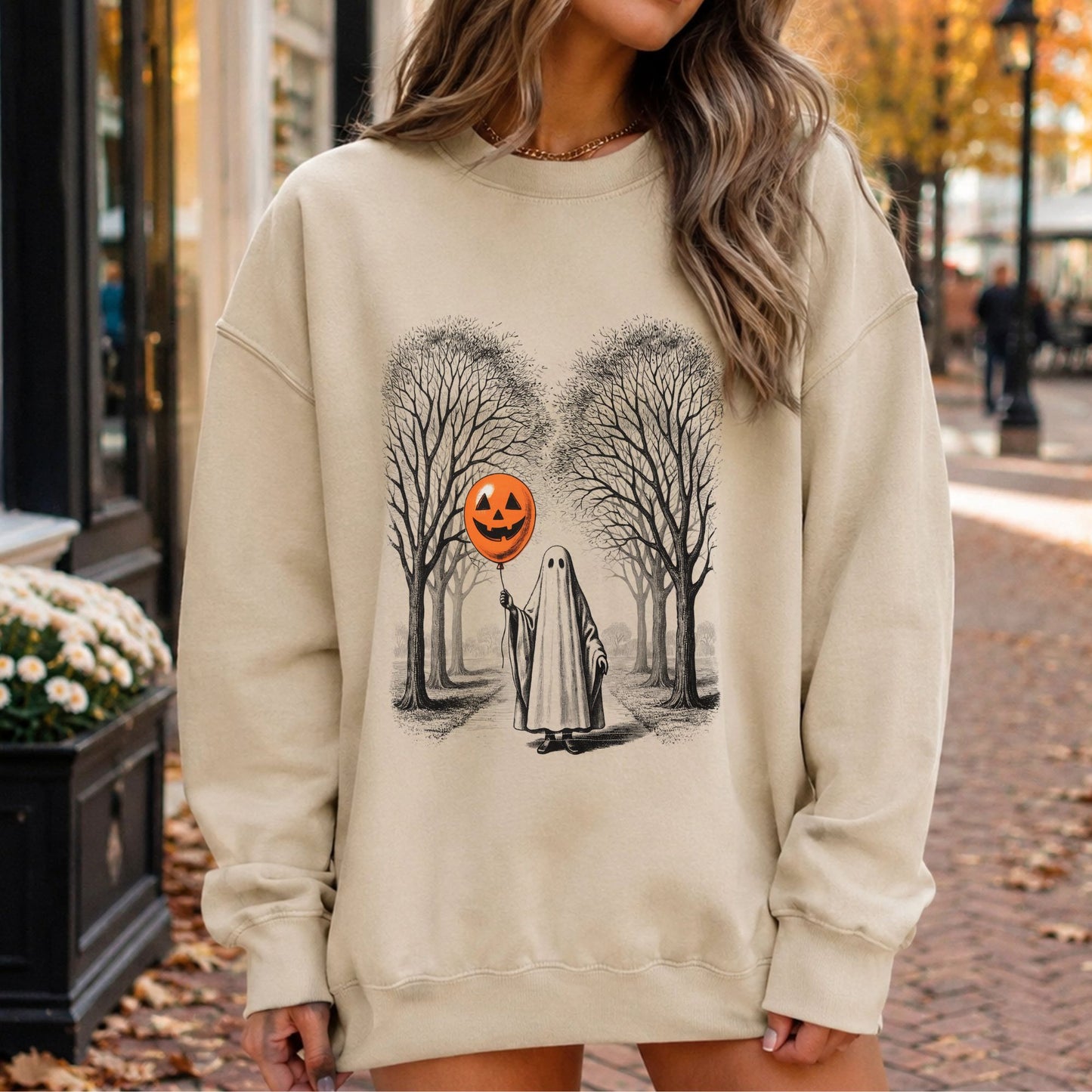Haunted forest Halloween DTF transfer featuring a mysterious sheet ghost walking through tall bare trees while holding an orange jack-o’-lantern balloon, displayed on a cream sweatshirt mockup.