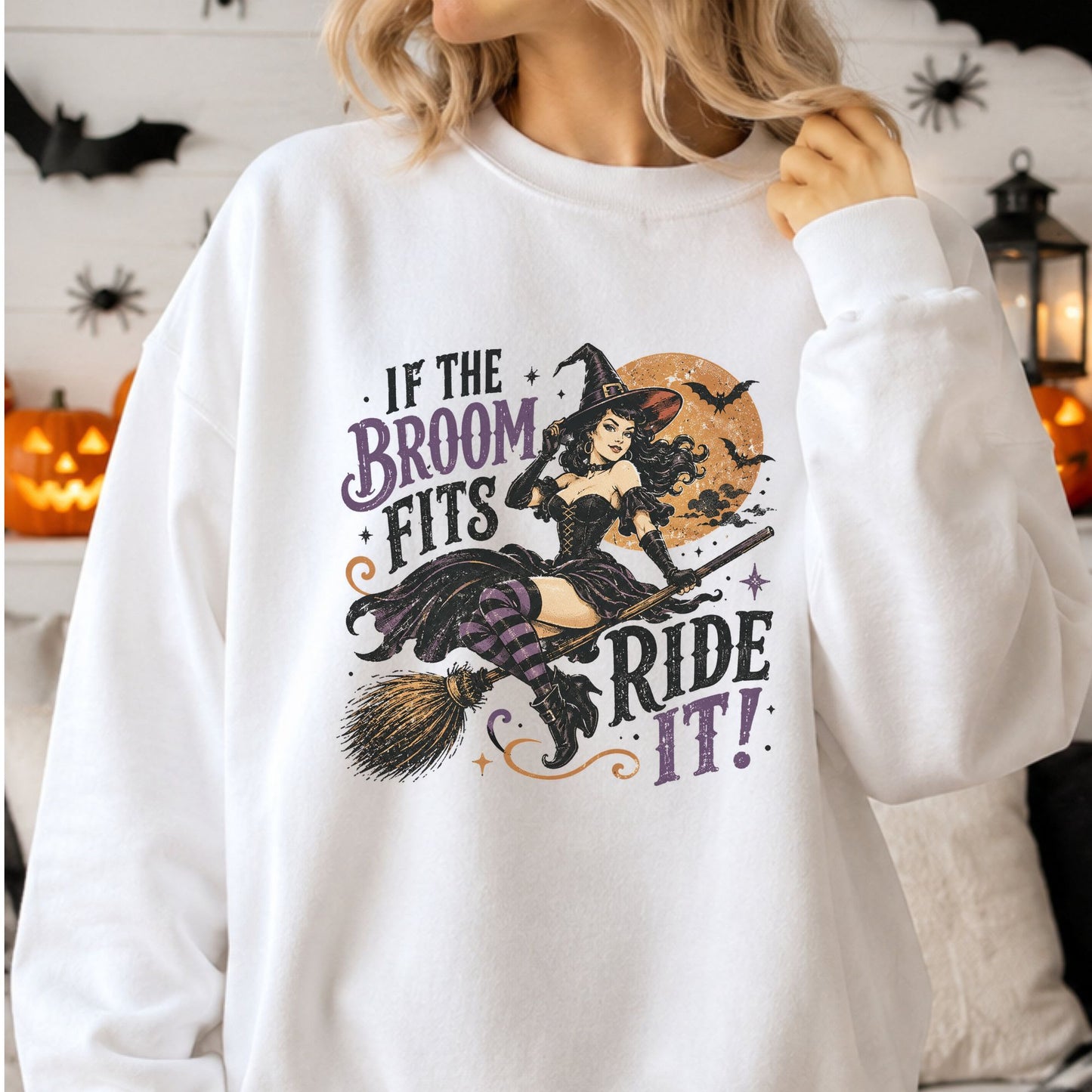 Vintage If the Broom Fits, Ride It Halloween DTF transfer featuring a glamorous pinup witch riding a broom beneath an orange full moon with flying bats, purple striped stockings and distressed retro lettering on a white sweatshirt mockup.