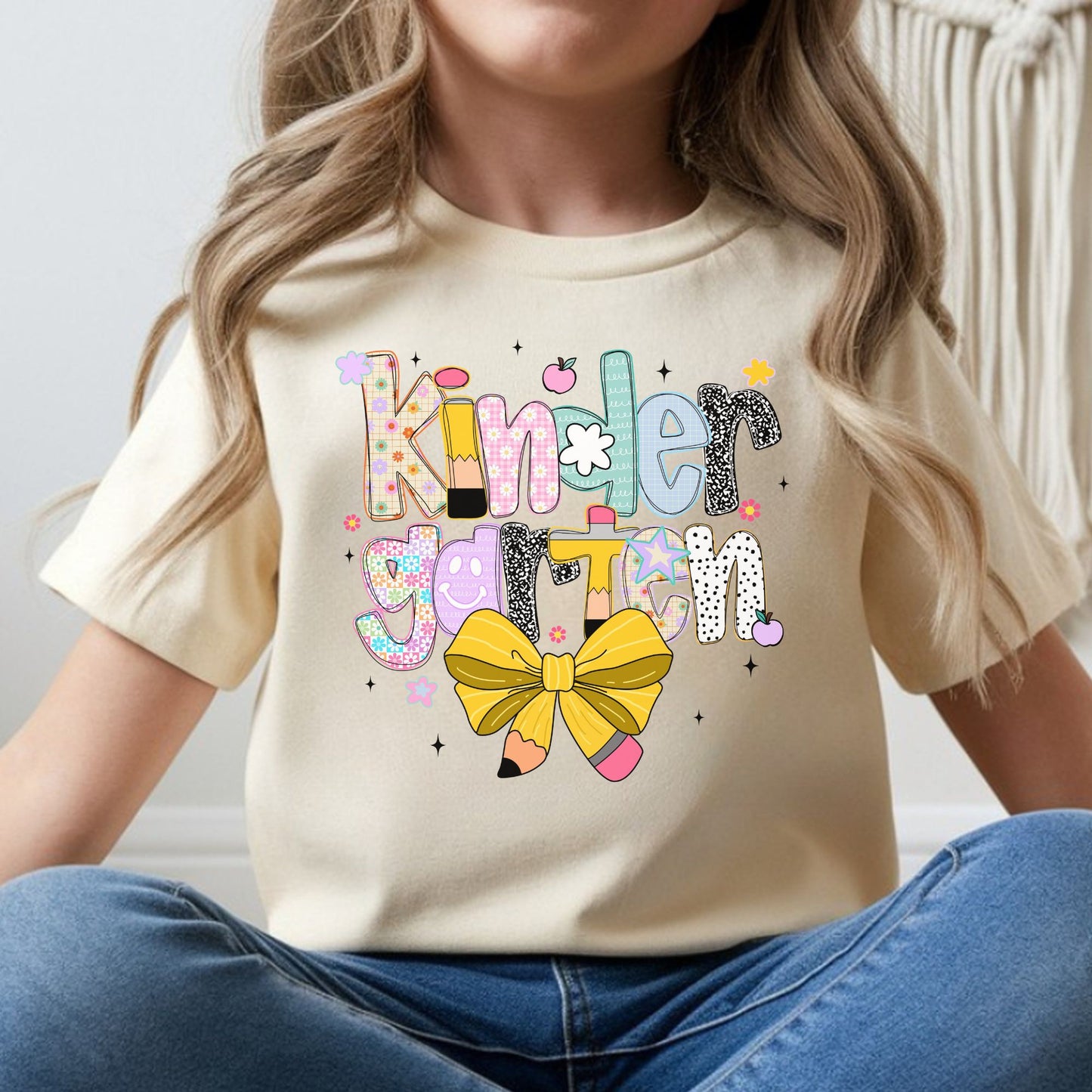 Kindergarten back-to-school design featuring colorful patterned letters, pencil accents, a yellow pencil bow, flowers, apples, and playful classroom details for kids shirts.