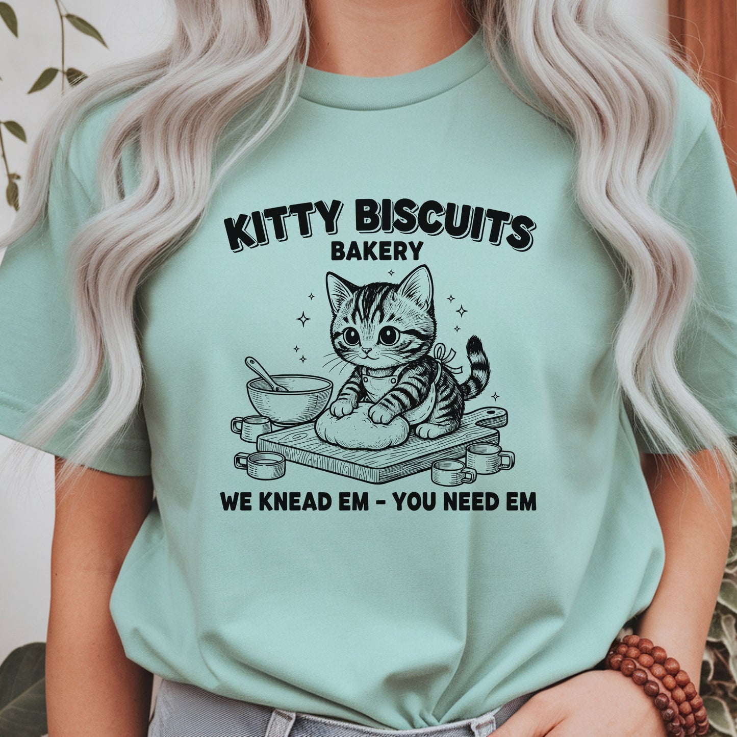 Cute kitten kneading dough with the phrase Kitty Biscuits Bakery We Knead Em You Need Em, funny cat baking design perfect for cat lovers, bakers, pet parents, and animal humor fans