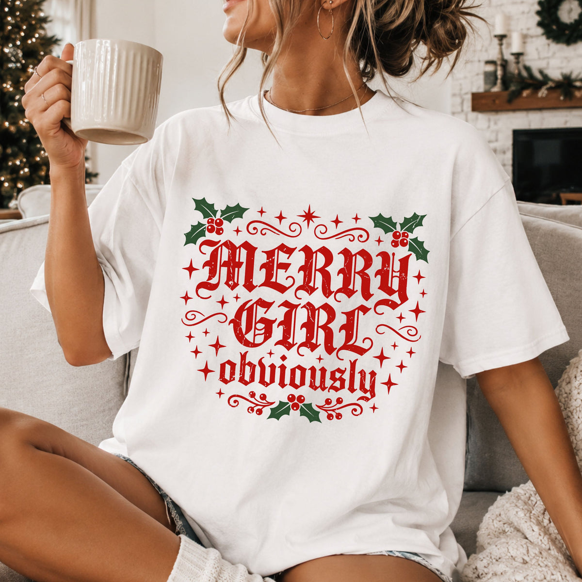“Merry Girl obviously” in distressed red Old English lettering surrounded by red starbursts, decorative flourishes and green holly leaves with red berries.