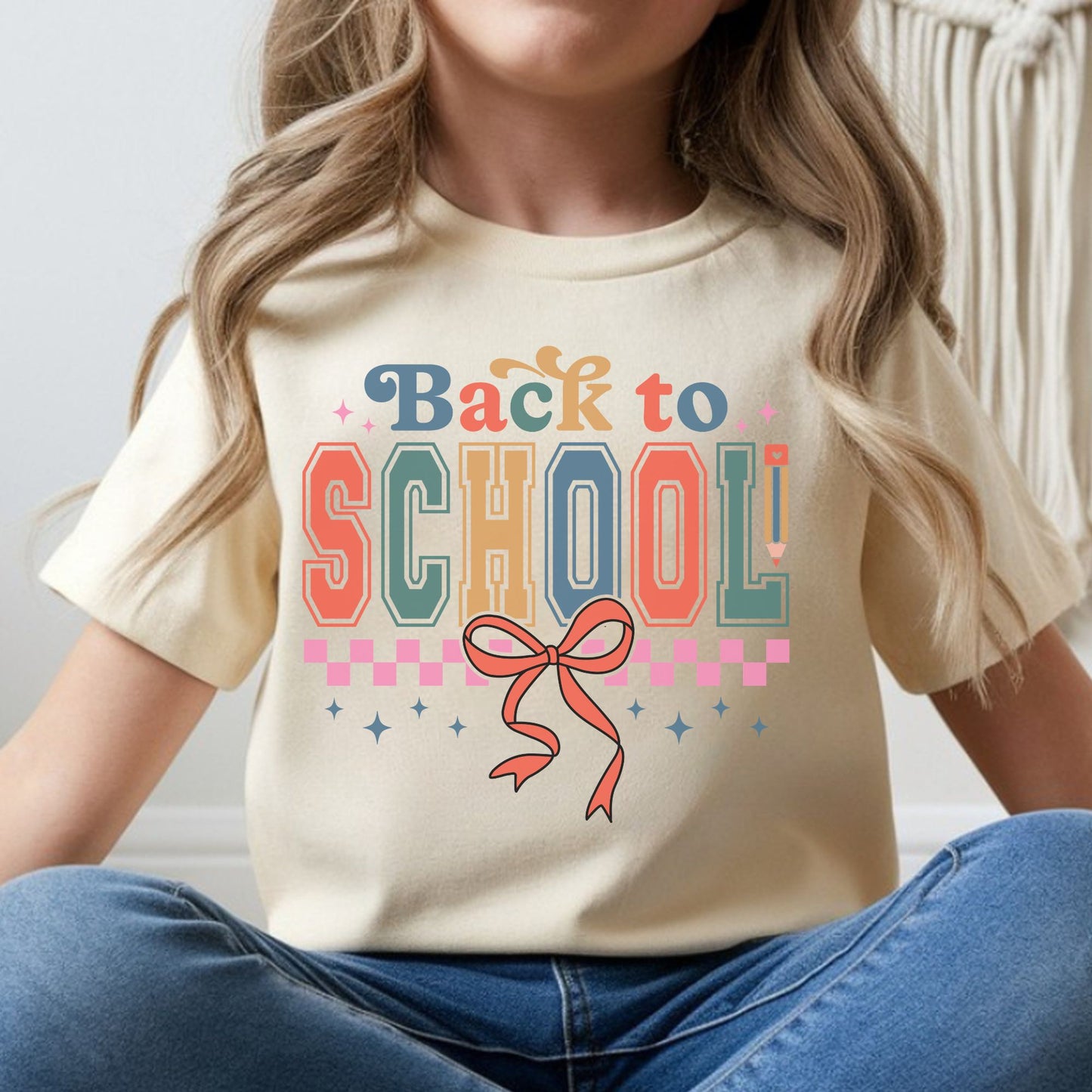 Retro back-to-school design featuring colorful collegiate-style lettering, a coral bow, pink checkerboard accents, sparkles, and a pencil detail for kids shirts.