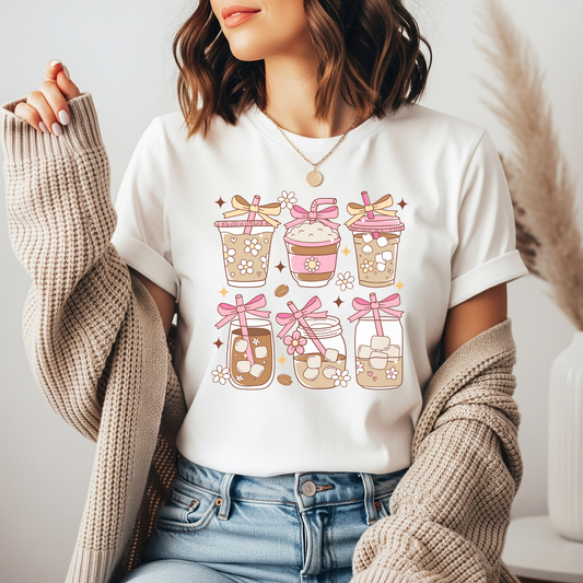 Person wearing a white t-shirt with a graphic design of coffee cups and bows.