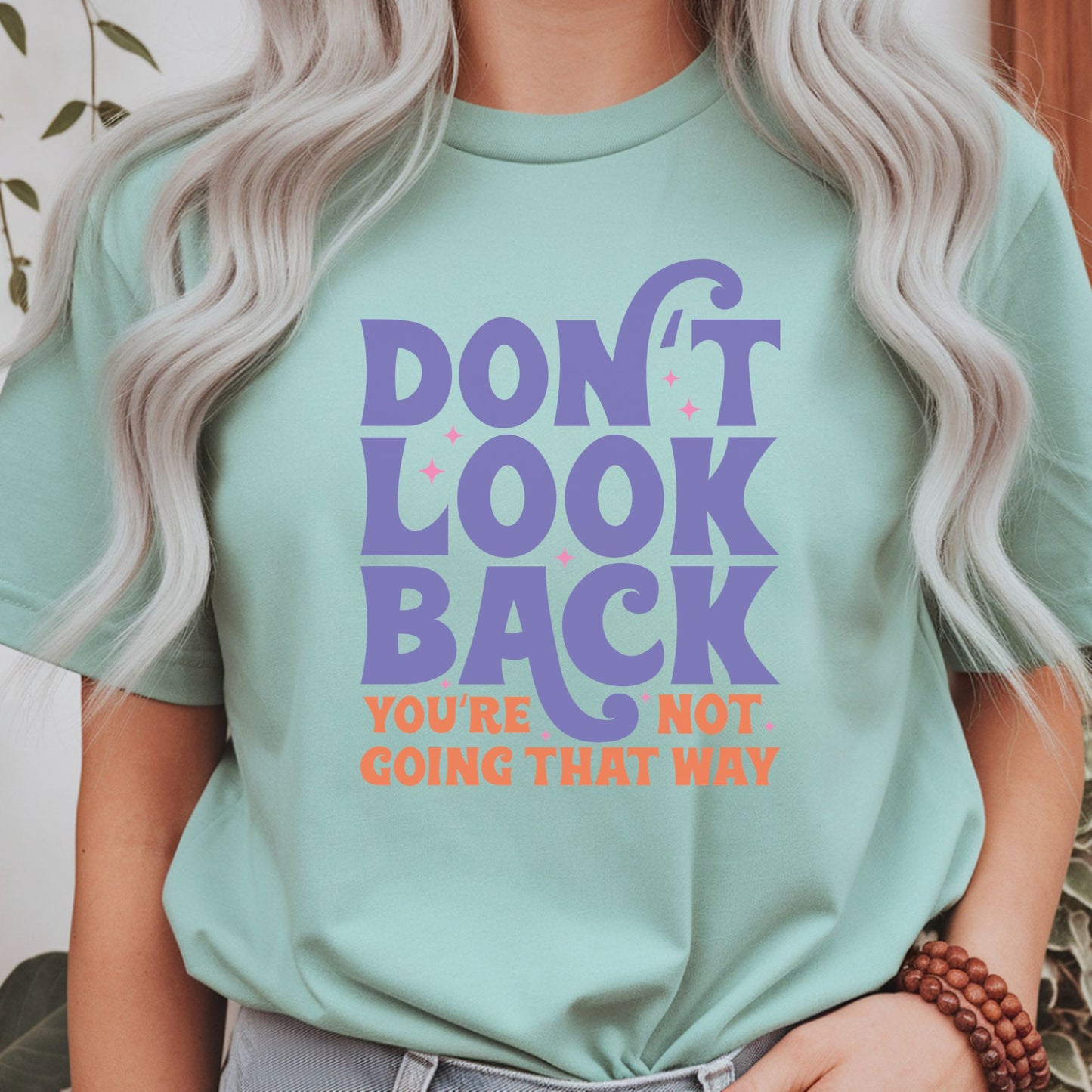 Motivational retro typography design featuring the quote Don't Look Back You're Not Going That Way in purple and orange lettering with pink sparkles