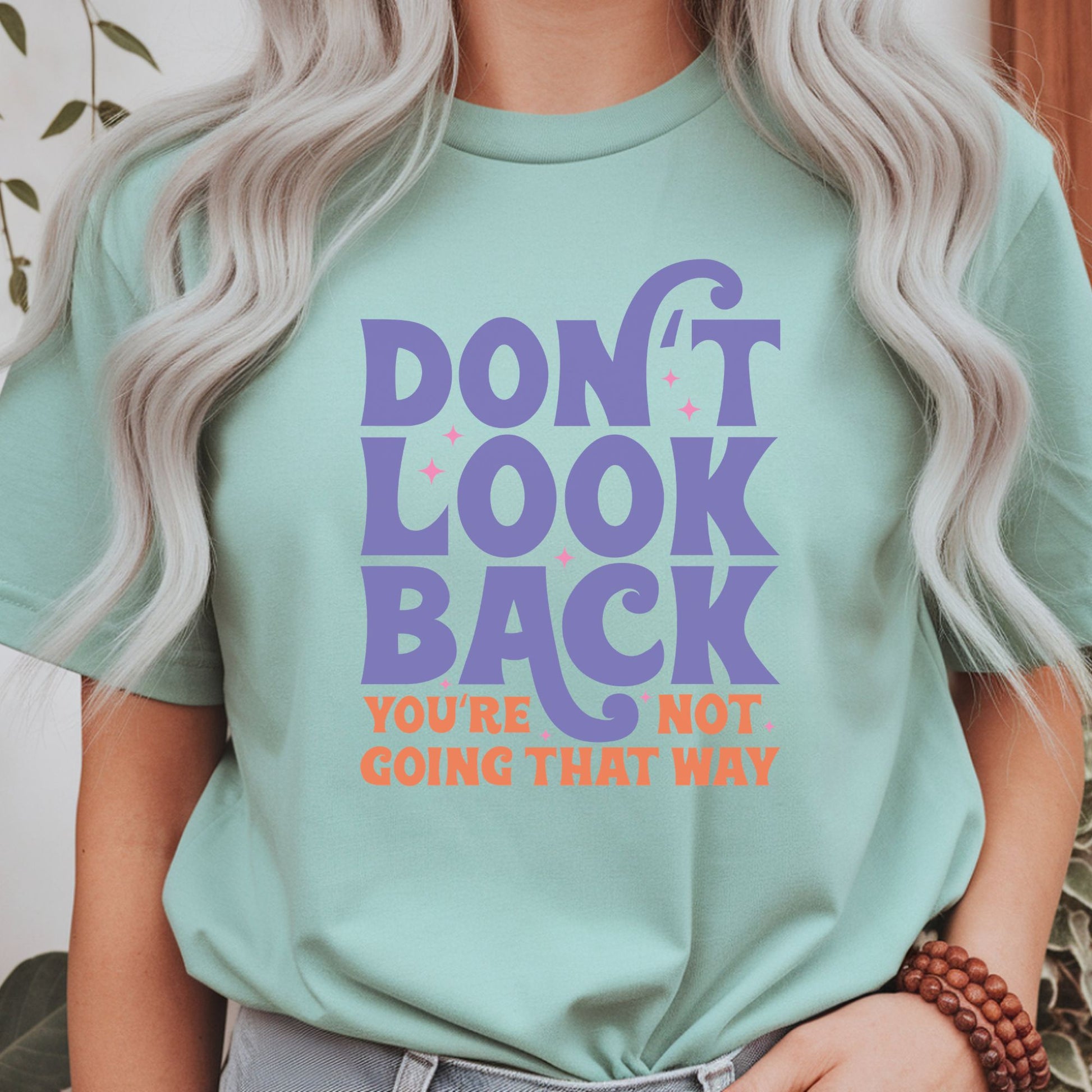 Motivational retro typography design featuring the quote Don't Look Back You're Not Going That Way in purple and orange lettering with pink sparkles