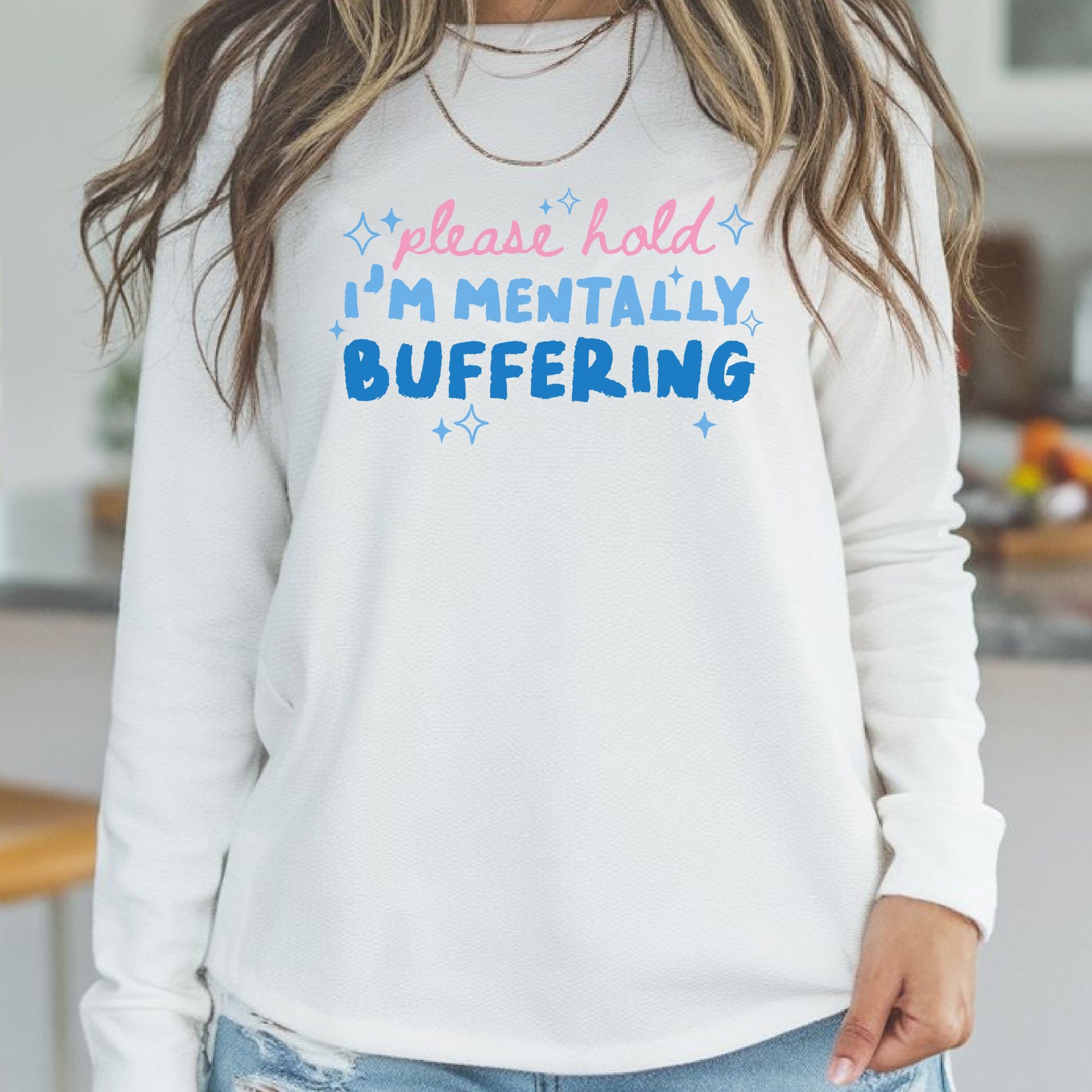 Funny Please Hold I'm Mentally Buffering graphic with pink script text, blue retro lettering, and sparkles on a white sweatshirt