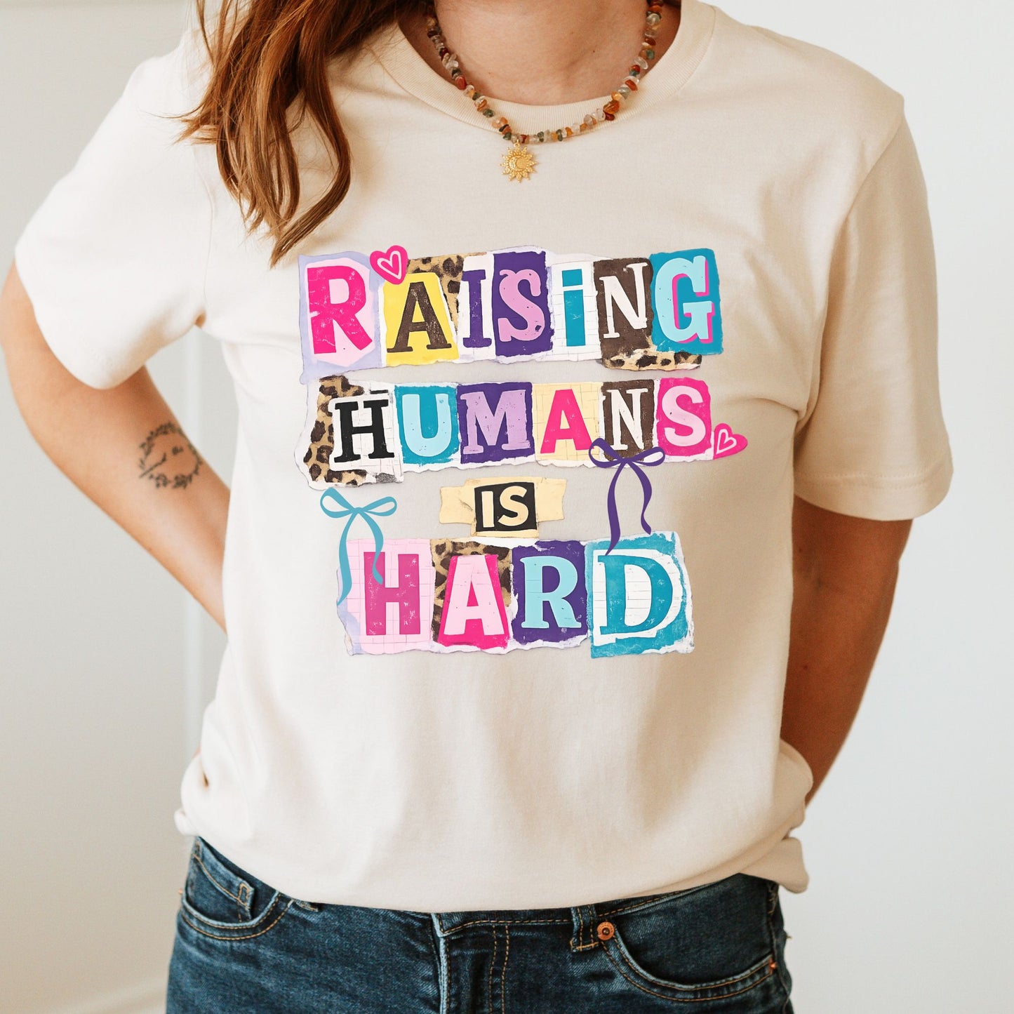 Raising humans is hard DTF transfer with colorful collage lettering, bows, hearts, and leopard print accents