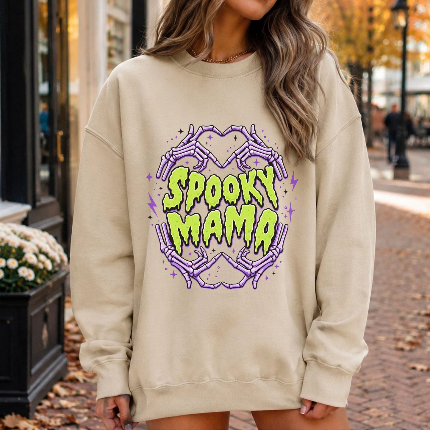 Spooky Mama Halloween DTF transfer featuring neon green dripping lettering surrounded by purple skeleton hands forming heart shapes, with black and purple stars, lightning bolts and sparkling accents on a cream sweatshirt mockup.