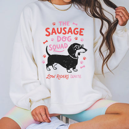 Funny dachshund graphic featuring a stylish sausage dog wearing sunglasses with the phrase The Sausage Dog Squad Low Riders Unite, surrounded by paw prints and bones in pink and coral tones