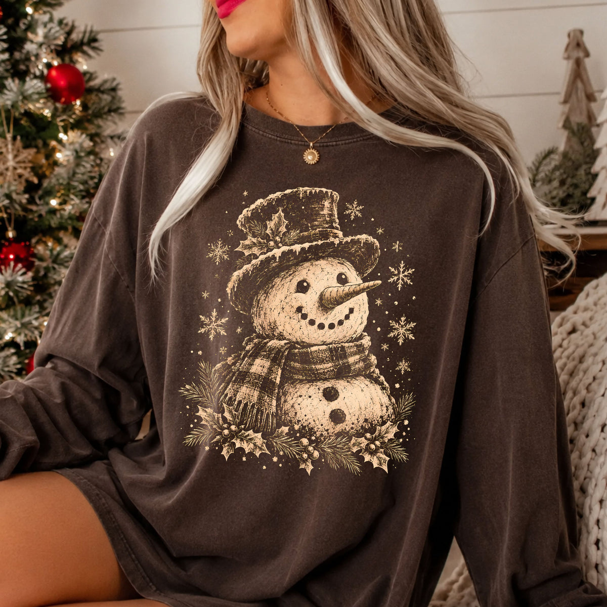 Vintage tan snowman wearing a top hat and plaid scarf, surrounded by snowflakes, pine branches, holly leaves and berries in a distressed sketch style.