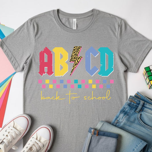 Colorful ABCD back-to-school design featuring distressed varsity letters, a leopard-print lightning bolt, checkerboard accents, and bright retro colors for kids shirts.