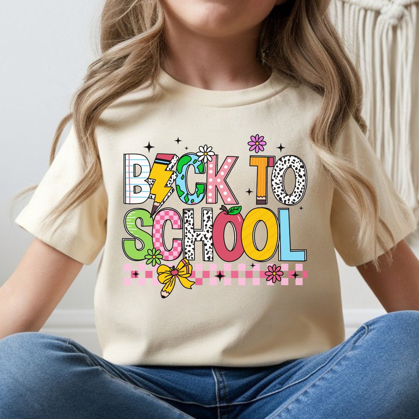 Colorful back-to-school design featuring bold mixed-pattern letters, a globe, pencil, apple, flowers, bow, lightning bolt, and pink checkerboard accents for kids shirts.