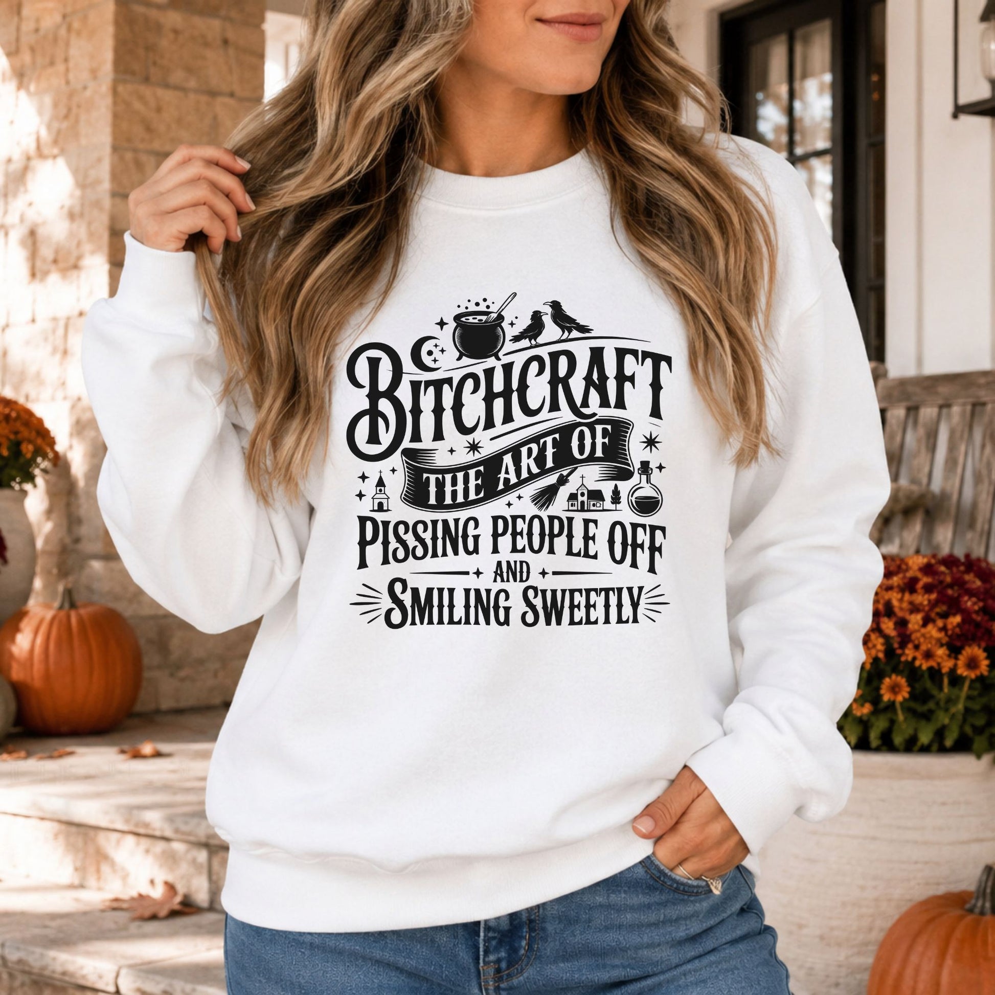 Black-and-white Bitchcraft Halloween DTF transfer featuring the quote The Art of Pissing People Off and Smiling Sweetly with a bubbling cauldron, crows, crescent moon, broom, potion bottle and witchy accents on a white sweatshirt mockup.