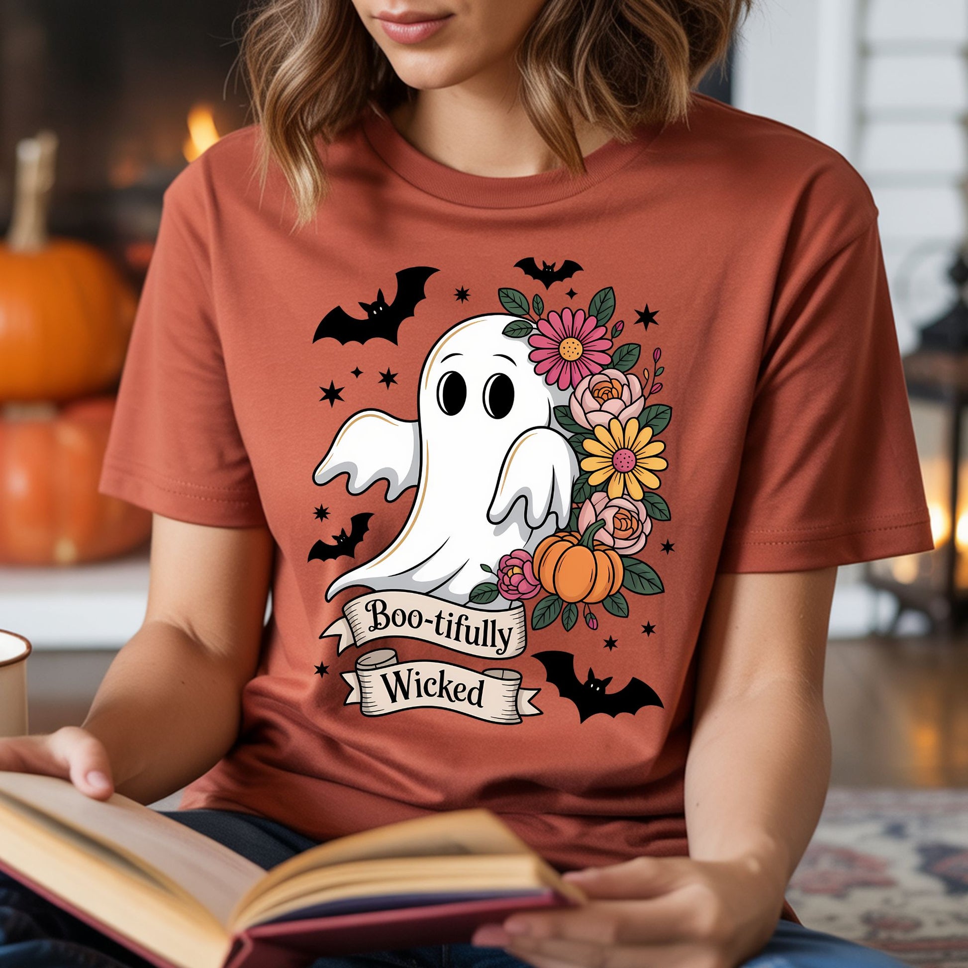 Boo-tifully Wicked Halloween DTF transfer featuring a cute white ghost surrounded by pink, orange and yellow flowers, green leaves, pumpkins, black bats and sparkling accents on a rust-colored T-shirt mockup.