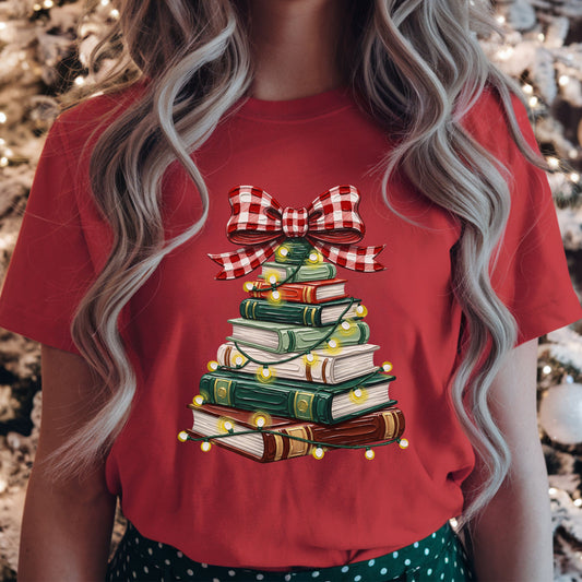 Green, red, cream and brown books stacked into a Christmas tree, wrapped in glowing string lights and topped with a large red and white gingham bow.