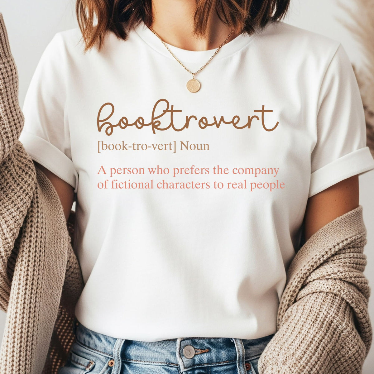 Booktrovert definition DTF transfer with the funny phrase “A person who prefers the company of fictional characters to real people” in neutral brown and coral lettering for book lover shirts, reader sweatshirts, and literary apparel.