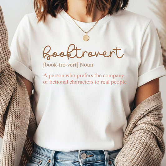 Booktrovert definition DTF transfer with the funny phrase “A person who prefers the company of fictional characters to real people” in neutral brown and coral lettering for book lover shirts, reader sweatshirts, and literary apparel.
