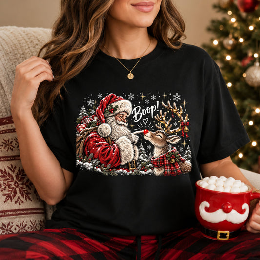 “Boop!” above Santa touching a reindeer’s red nose, surrounded by snowy trees and snowflakes. The reindeer wears a red plaid scarf and has lights, a bow and bells on its antlers.