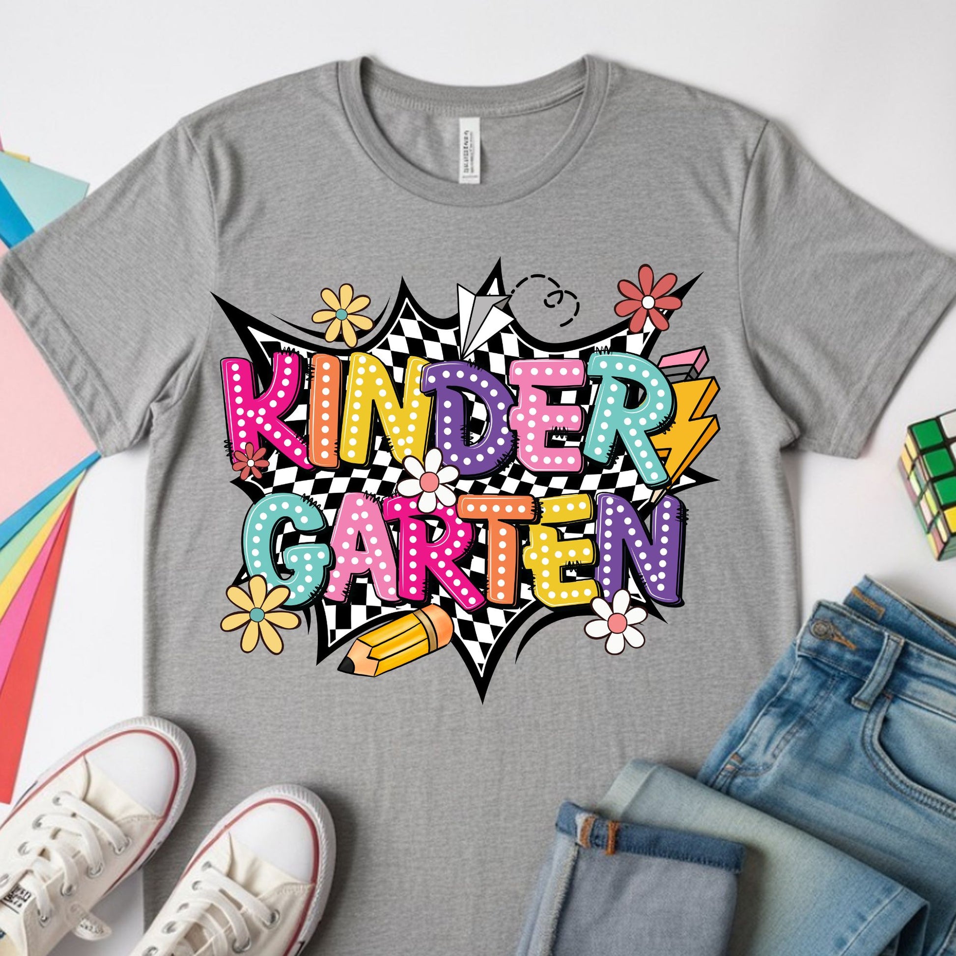 Colorful Kindergarten back-to-school design featuring bright bubble letters, black-and-white checkerboard accents, flowers, a pencil, paper airplane, lightning bolt, and playful classroom graphics.