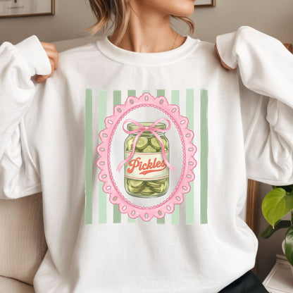 Cute coquette pickle jar graphic featuring a vintage pickle jar, pink bow, scalloped frame, and green striped background for trendy graphic tees, hoodies, and preppy apparel.
