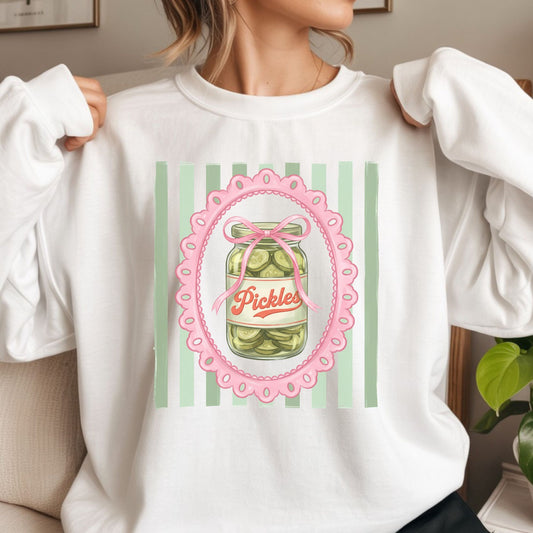 Cute coquette pickle jar graphic featuring a vintage pickle jar, pink bow, scalloped frame, and green striped background for trendy graphic tees, hoodies, and preppy apparel.
