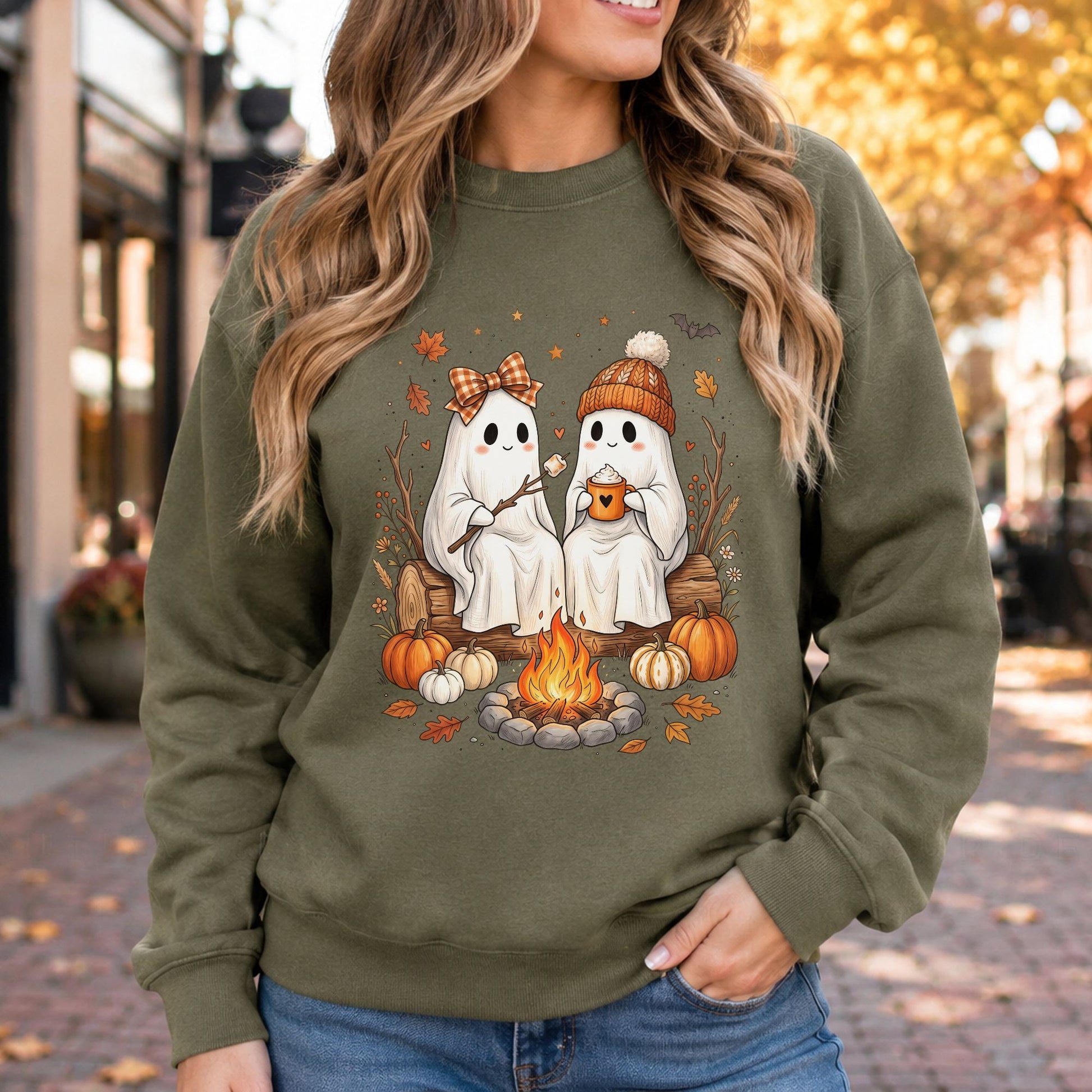 Cozy fall ghost DTF transfer featuring two cute ghosts sitting beside a campfire with hot cocoa, marshmallows, pumpkins, autumn leaves, a knit hat and a gingham bow on an olive green sweatshirt mockup.
