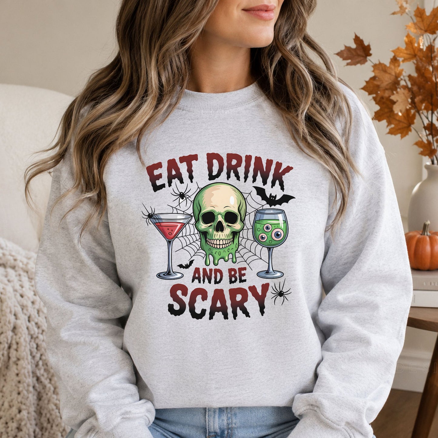 Eat, Drink and Be Scary Halloween DTF transfer featuring a dripping green skull between red and green spooky cocktails with floating eyeballs, spiderwebs, bats and black spiders on a gray sweatshirt mockup.