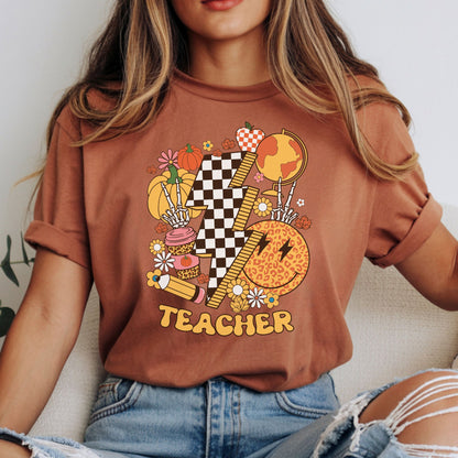 Fall teacher design featuring a black and white checkerboard lightning bolt, autumn pumpkins, globe, ruler, pencil, leopard smiley face, coffee cup, flowers, skeleton hands, and warm retro colors.