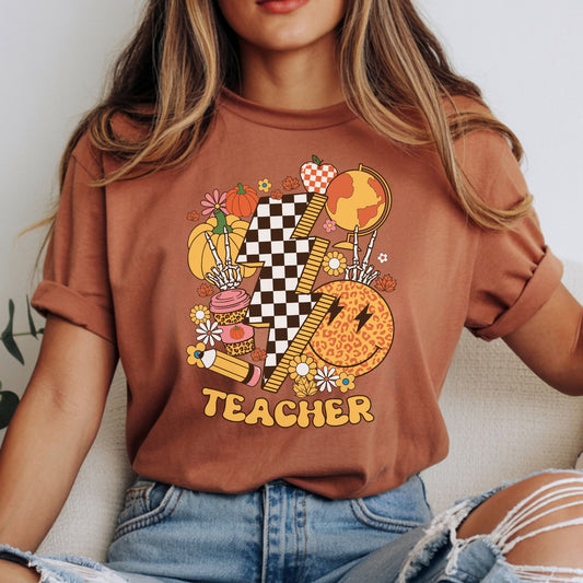 Fall teacher design featuring a black and white checkerboard lightning bolt, autumn pumpkins, globe, ruler, pencil, leopard smiley face, coffee cup, flowers, skeleton hands, and warm retro colors.