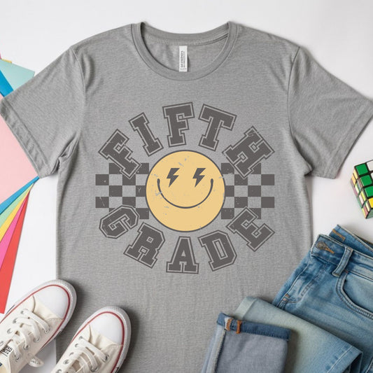 Fifth Grade back-to-school design featuring distressed collegiate lettering, a yellow smiley face with lightning-bolt eyes, and bold black checkerboard accents for kids shirts.