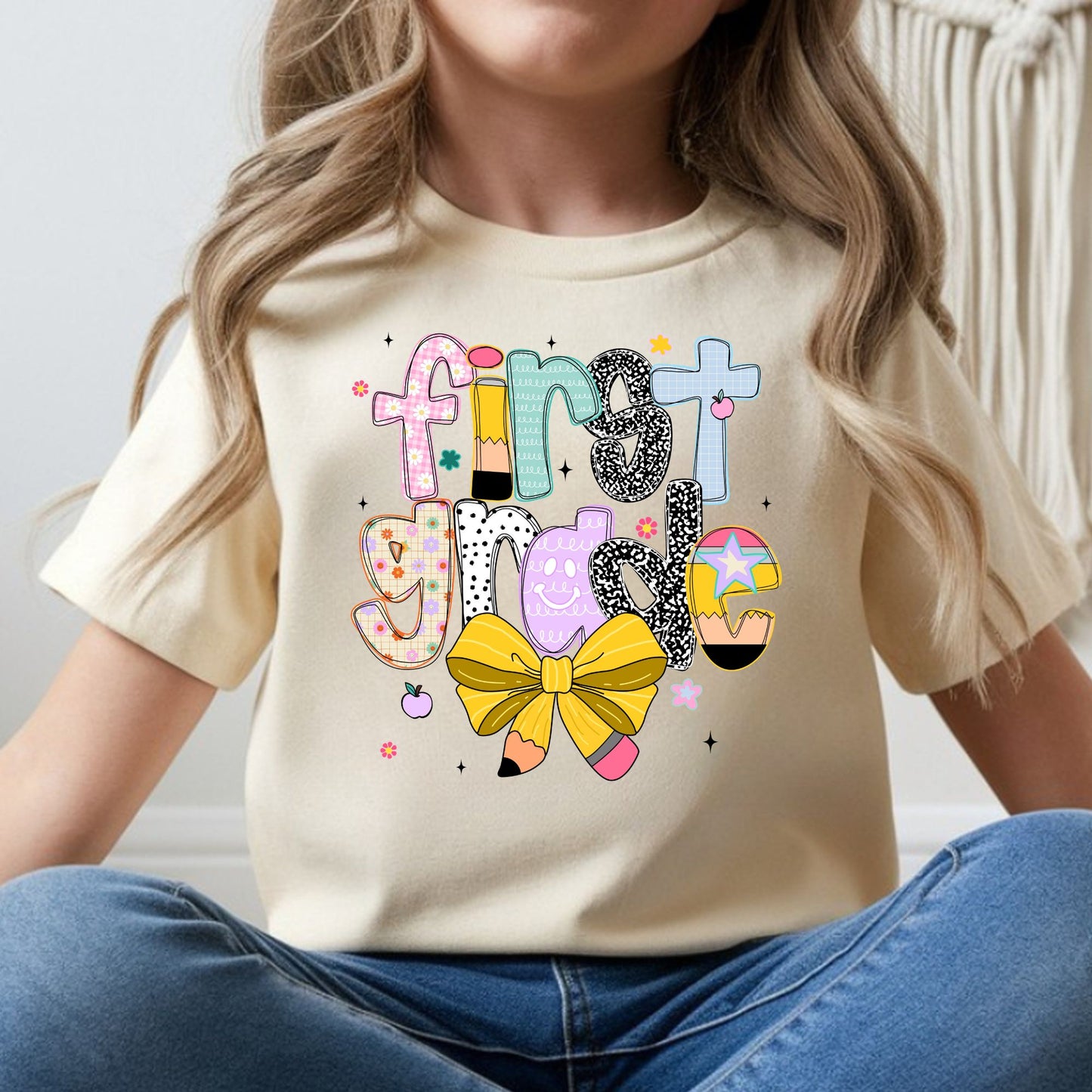 First Grade back-to-school design featuring colorful patterned letters, pencil accents, a yellow pencil bow, flowers, apples, and playful classroom details for kids shirts.