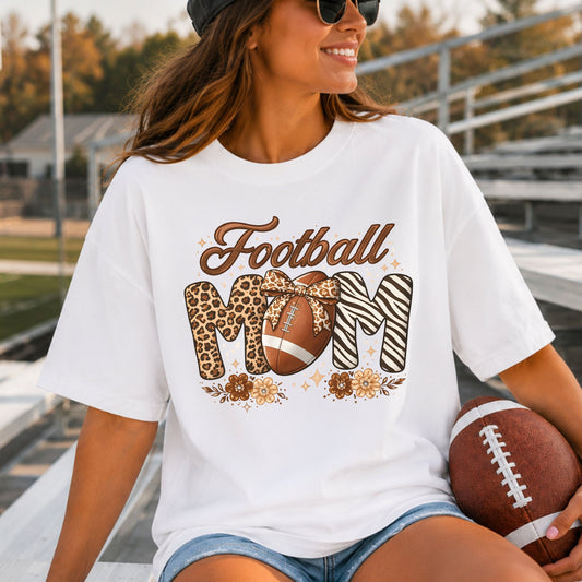 Football Mom DTF transfer featuring brown script Football lettering, leopard print and zebra print MOM letters, a football with leopard bow, neutral flowers, and sparkle accents.