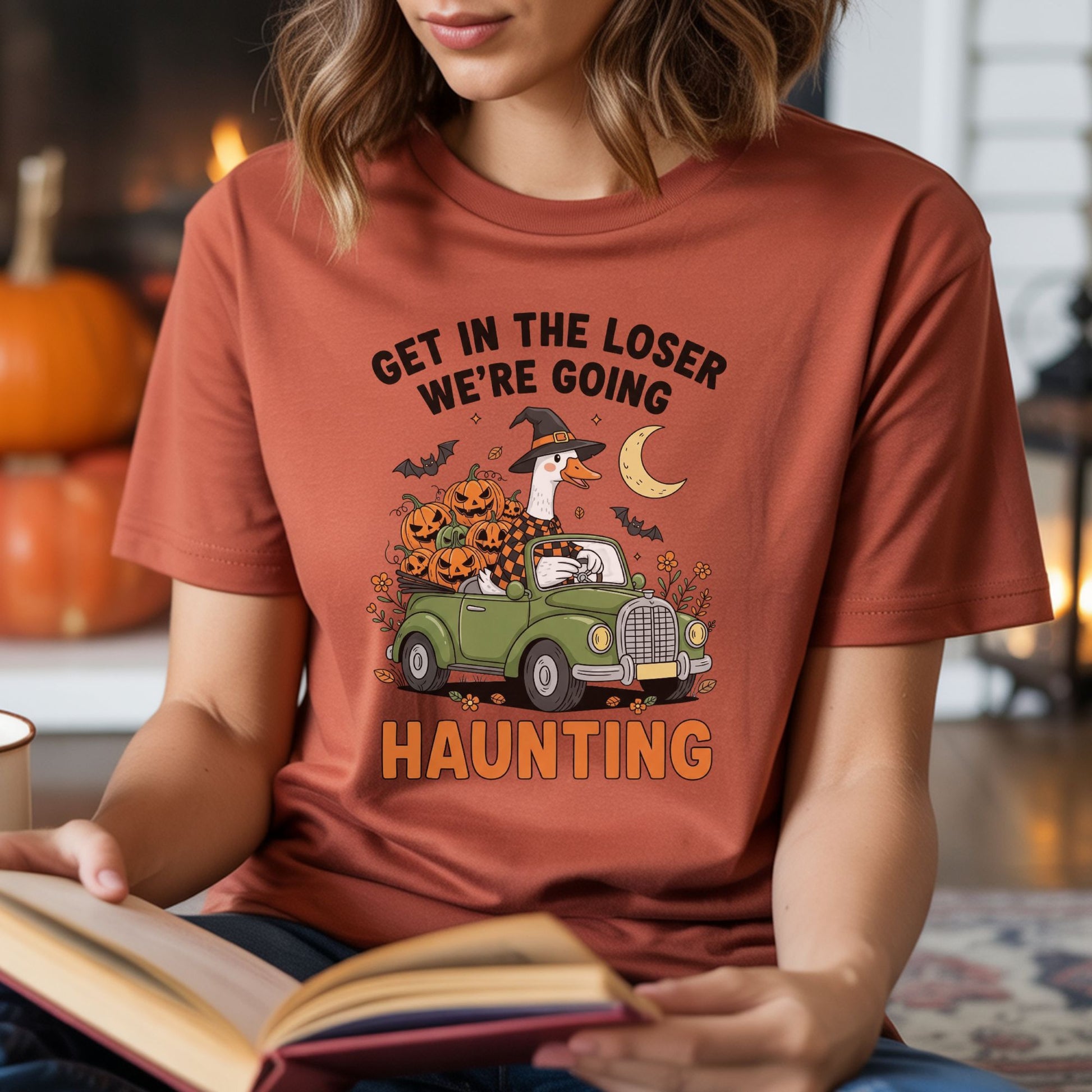 Funny Halloween DTF transfer featuring a witch goose driving a green vintage convertible filled with jack-o-lantern pumpkins beneath a crescent moon, surrounded by bats, flowers and fall leaves with the phrase Get in the Loser, We’re Going Haunting.