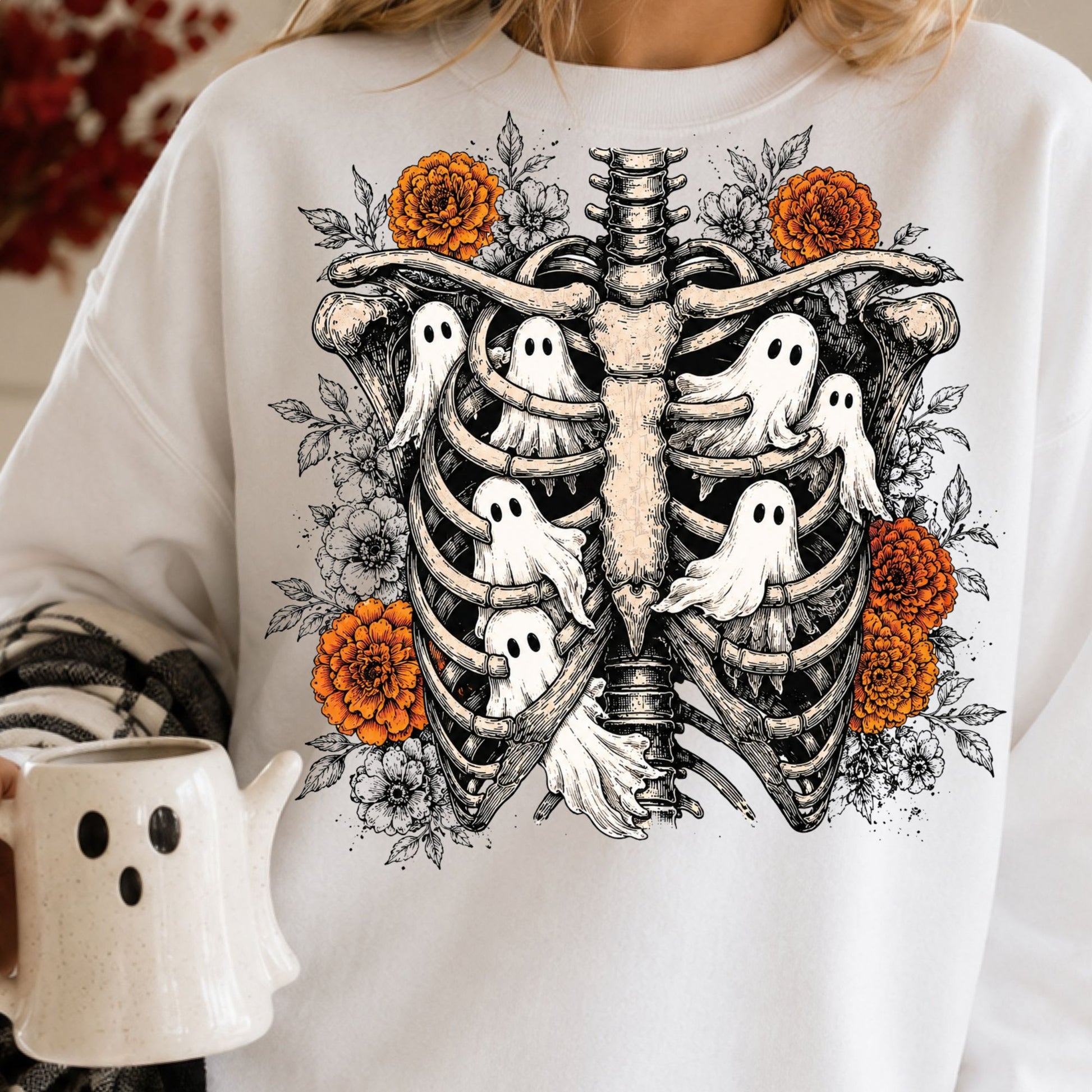 Gothic Halloween DTF transfer featuring a detailed skeletal ribcage filled with cute white ghosts and surrounded by orange marigolds, black-and-white flowers and leafy botanical accents on a white sweatshirt mockup.