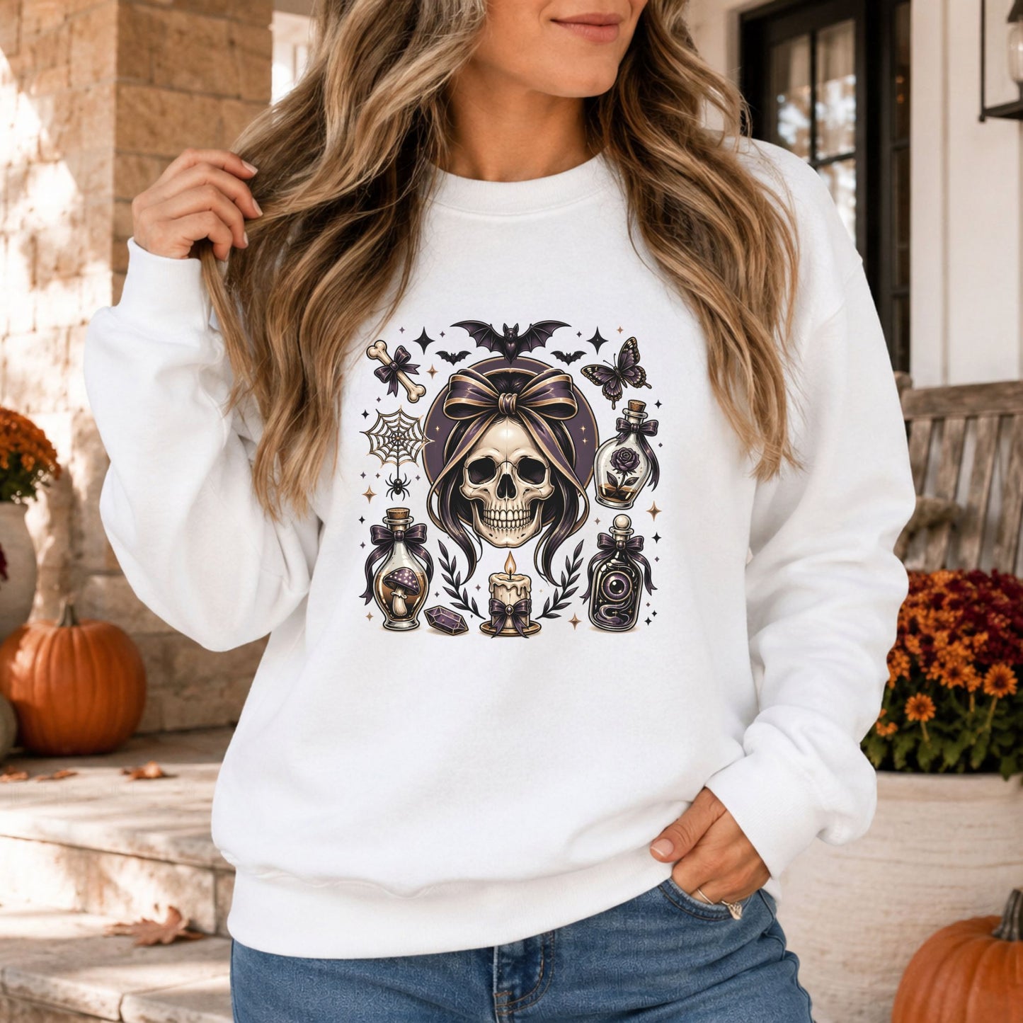 Gothic coquette Halloween DTF transfer featuring a detailed skull framed by dark hair and an oversized black bow, surrounded by poison bottles, bats, a spiderweb, butterfly, candle, mushroom, crystal and sparkling accents on a white sweatshirt mockup.