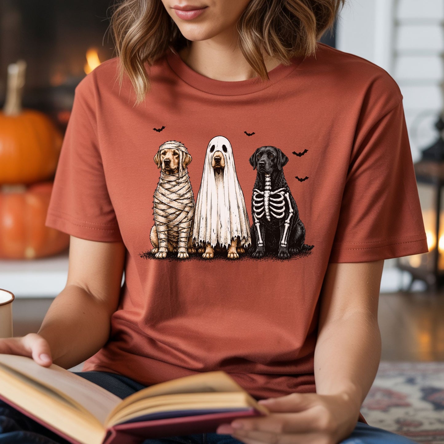 Halloween dog DTF transfer featuring three realistic dogs dressed in mummy, sheet ghost and skeleton costumes with flying black bats, displayed on a rust-colored T-shirt mockup.