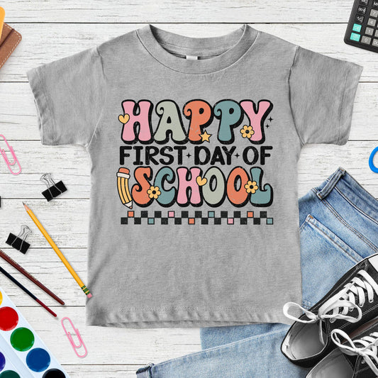 Happy First Day of School design featuring colorful retro lettering, a pencil, flowers, hearts, stars, and checkerboard accents for toddler, kids, and youth shirts.