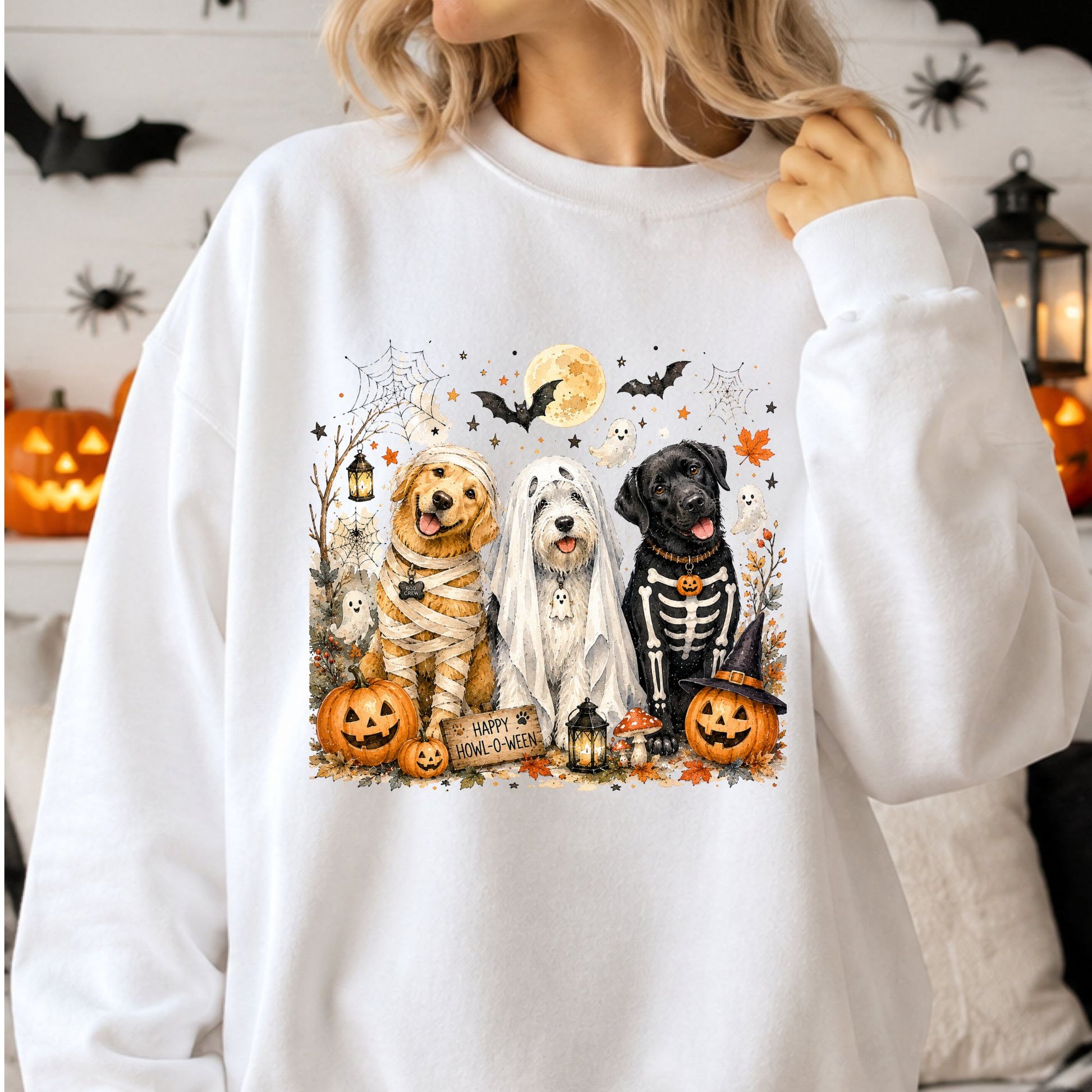 Happy Howl-O-Ween Halloween DTF transfer featuring three dogs dressed in mummy, sheet ghost and skeleton costumes, surrounded by jack-o’-lanterns, bats, spiderwebs, lanterns, fall leaves and a glowing full moon on a white sweatshirt mockup.