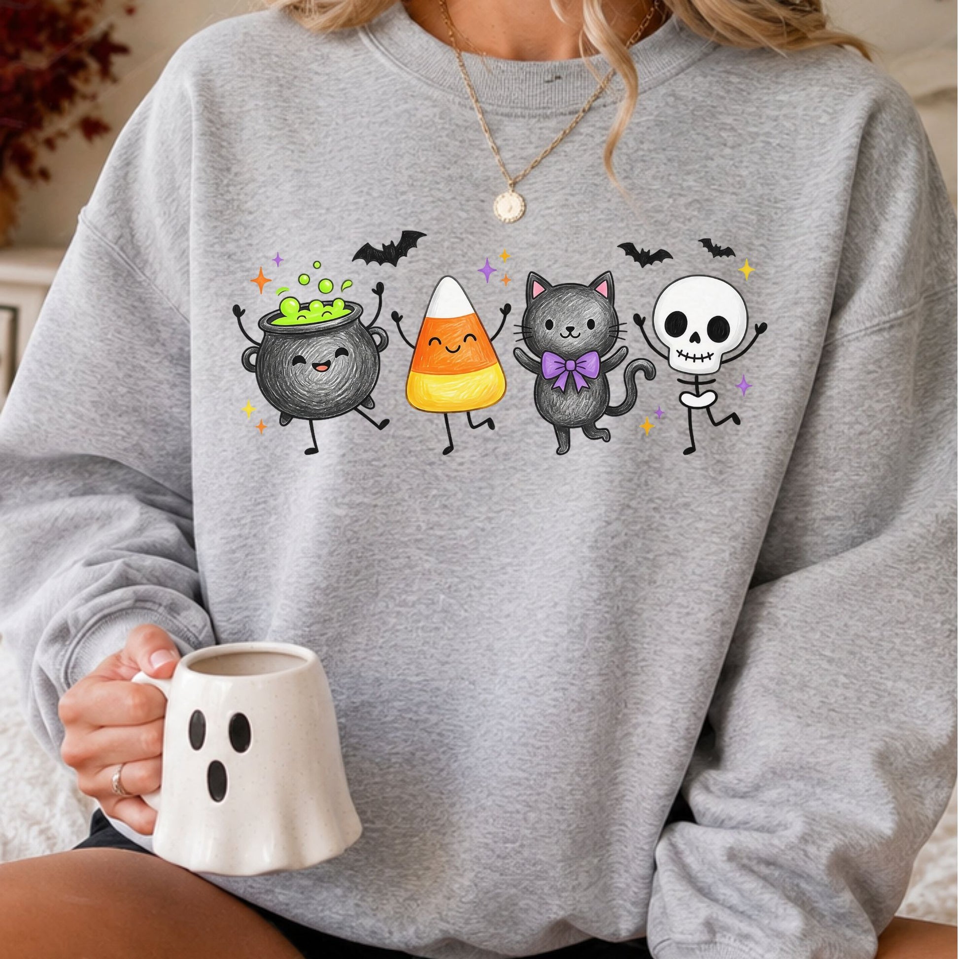 Cute Halloween DTF transfer featuring a smiling bubbling cauldron, candy corn, black cat with a purple bow and dancing skeleton character, surrounded by colorful stars and flying bats on a gray sweatshirt mockup.