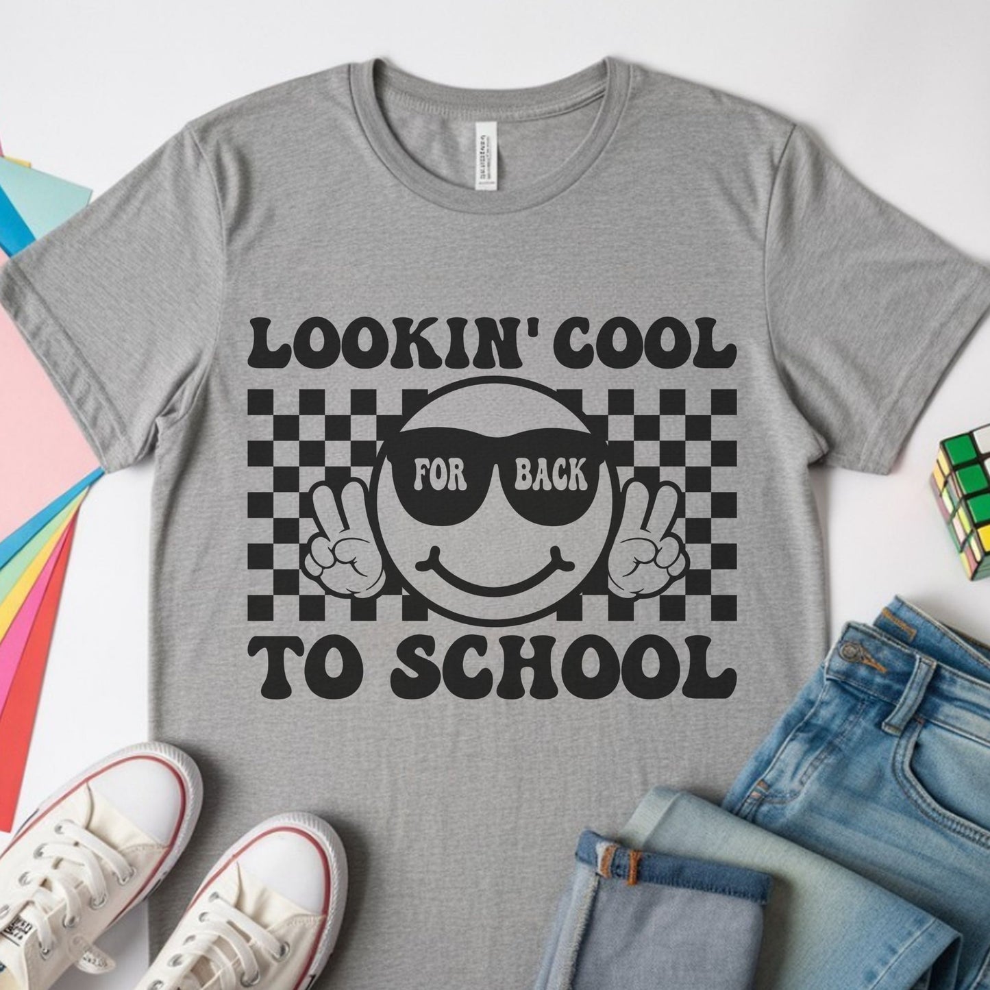 Lookin’ Cool for Back to School design featuring a smiling face in sunglasses, peace-sign hands, and a bold black checkerboard background for kids shirts.