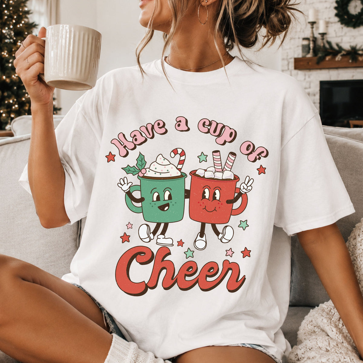 “Have a Cup of Cheer” with smiling green and red hot cocoa mugs, whipped cream, marshmallows, a candy cane and stars in a distressed retro style.